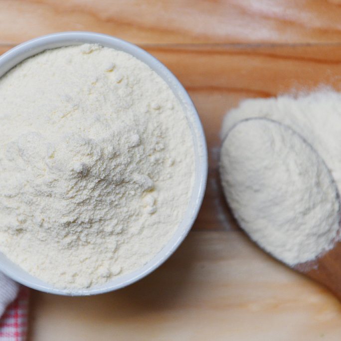 Milk powder in spoon and cup for baby on wooden table